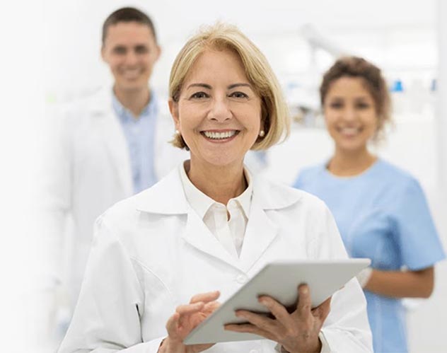 Eine lächelnde Zahnärtzin mit ihren Dental-Hygieniker:innen in einem Praxisraum